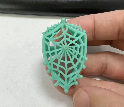 Green wax jewelry pattern with openwork details held between fingers